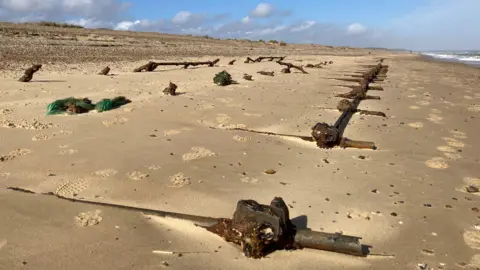 Dave Thurlow The remains of World War Two scaffolding poles emerging from sand at Minsmere in Suffolk. They formed the base of wartime defences. The metal poles are in a grid with a long section running parallel with the sea, while other poles are set at right angles, are still largely submerged and are and locked into position by joints. On the far right, the sea can just be glimpsed.