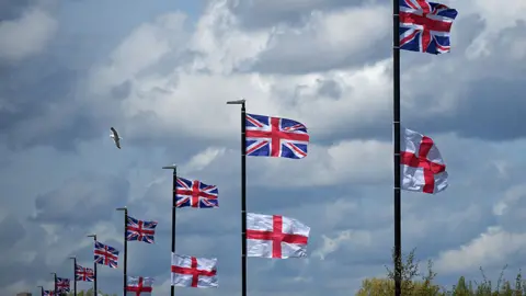 Getty Images Lamp-posts with union jacks flying from the top, with England flags slightly below them. A cloudy sky is in the background