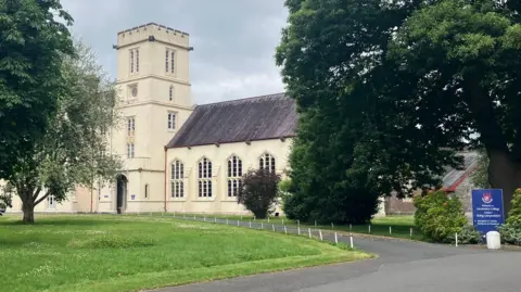 An old cream stone building in grounds with a blue sign saying Welcome to Llandovery College in English and in Welsh at the end of the drive.