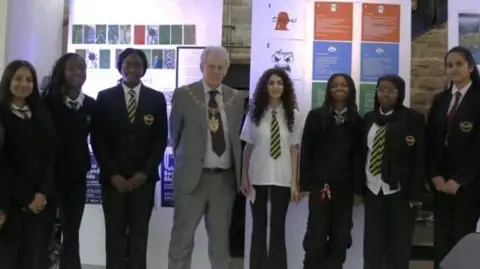 Lyng Hall School Lord Mayor Roger Bailey is wearing a light grey suit with a mayoral chain around his neck, He is flanked by students from Lyng Hall School on the opening night on their Beyond the Blade exhibition at the LTB Showrooms.