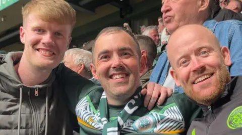 Cian O'Hara Three men are smiling at the camera. They are each wearing Celtic merchandise. 