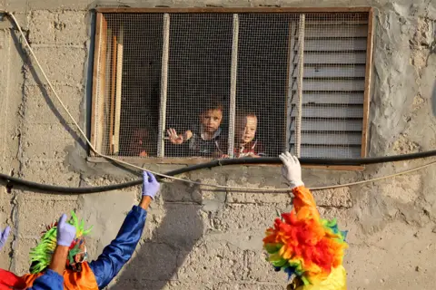 Ibraheem Abu Mustafa / Reuters Clowns wave at children who look out of a window