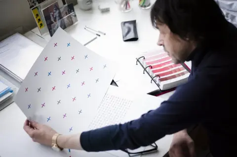 Umbro Peter Saville CBE looking at the multicoloured cross pattern on a sheet of paper