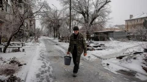 Reuters Man carries water through snow-covered Ukrainian street