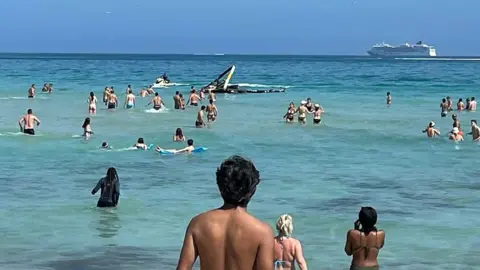 Beachgoers swim towards the crashed helicopter