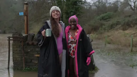 Charlotte Sawyer Charlotte Sawyer and Aggie Nyagari standing by the Avon. They are wearing swimsuits with smim robes over the top. They are smiling and looking into the camera