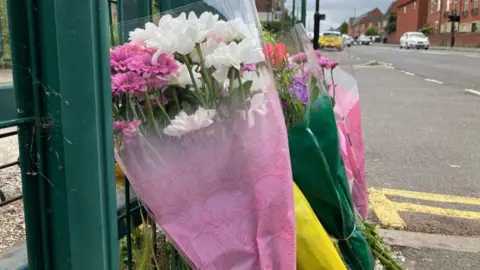 Flowers left at the scene as a tribute, with colours such as pink, yellow and green, placed next to a green railing