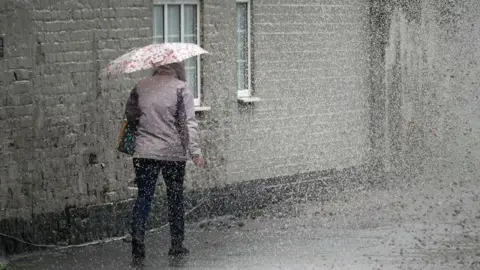 A pedestrian negotiates a partially flooded footpath as heavy rain begins on May 22, 2024 in Northwich, United Kingdom. 