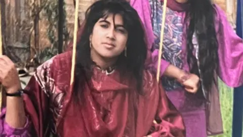 Teenage girl sitting on swing wearing a red dress, looking up at the camera.