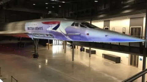 Adam Postans A Concorde model displayed in a museum, illuminated under bright lights