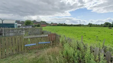 Google A Google Street View screengrab of the land where the homes would be built at Grange Farm. The site is a grassed area bordered by housing estates.