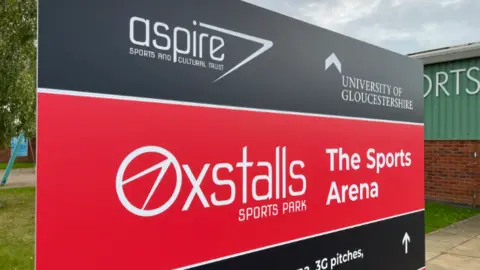 A red and grey sign of Oxstalls Sporks Park
