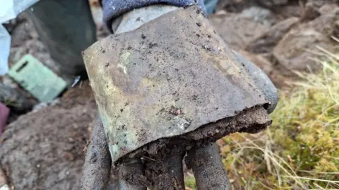 NTS The metal part has been flattened and is green in colour and has mud on it. 