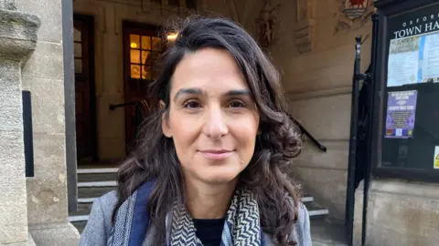 Dr Hosnieh Djafari-Marbini stood outside of Oxford town hall. She is wearing a scarf and grey jacket.