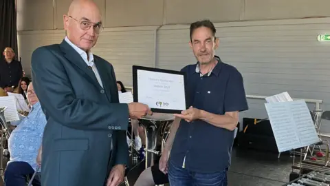 Two men are standing holding a picture frame which contains the words "Certificate of Honorary Membership presented to Andrew Keirl for donation and support. 