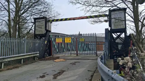 LDRS The bridge has a tarmac surface, gates, barriers, trees and a sign that read "WP Please Drive Carefully WP".