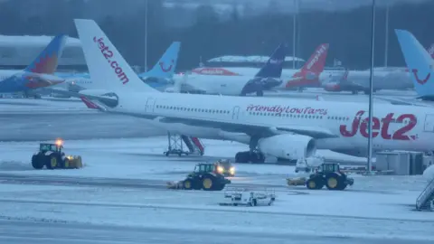 Staff use tractors to help clear snow from around aircraft after overnight snowfall caused the temporary closure of Manchester Airport