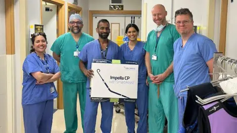 Sheffield Teaching Hospitals NHS Foundation Trust A group of doctors in blue and green scrubs huddle together on a ward