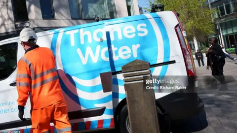 Getty Images Side of Thames Water van with employee in orange workwear seen from the rear. 