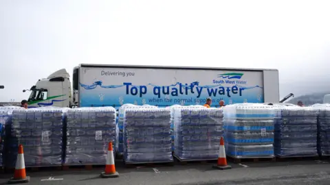PA Media A lorry that says "top quality water" parked behind pallets of water