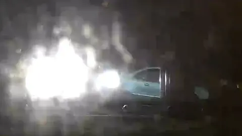 Paul Bright lights are on the left of a mainly dark image. Part of a blue car is on the right of the photo.