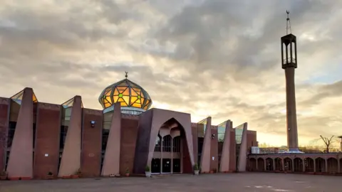 Exterior of Glasgow Central mosque - red stone building with lit dome and a paved courtyard