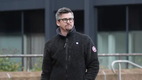 Joey Barton, with a beard, glasses and short hair, outside Liverpool Crown Court.