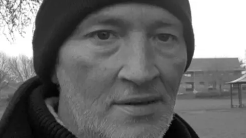 South Yorkshire Police A black and white image of a man, with a short white beard and a black woolly hat.