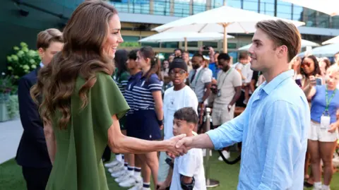 The Princess of Wales, wearing an olive green dress, shakes Arthur Fery hand.