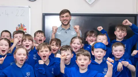 Cheering students in blue uniforms standing in front of Everton player Kiernan