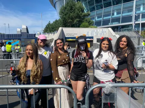 BTS fans holding up lightsticks and bottles of water as they queue to see the band at Tottenham Hotspur Stadium