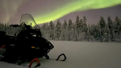 Danny Welch A sledge resting on snow with trees and the pink and green of the Northern lights in the star scattered sky beyond. 
