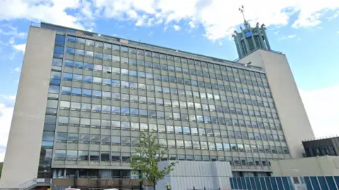 An exterior view of Newcastle Civic Centre, a large building with glass windows and an ornate tower on its right side.