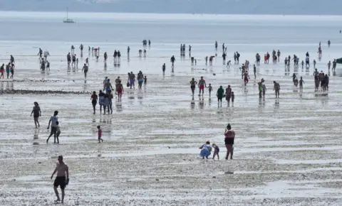 Getty Images People walk out at low tide into the sea as they gather to enjoy the warm sunny weather on Jubilee beach on July 18, 2021 in Southend-on-sea, England.