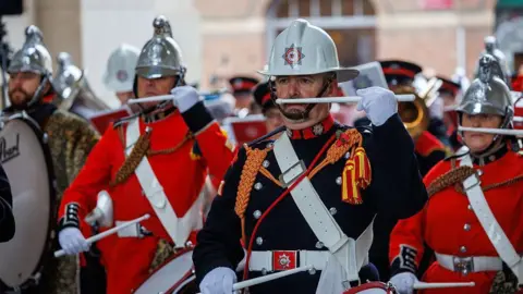 Getty Images Members of Devon and Somerset Fire and Rescue Service are marching in uniform and white hard hats, some playing the drums.