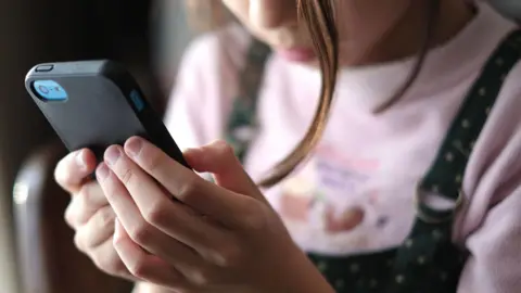 A stock image of a young child - face partially obscured - holding a phone