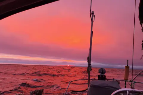 Mags Blyth A vast pink sunrise above the water, which is reflecting the colour, is captured from on board a boat.