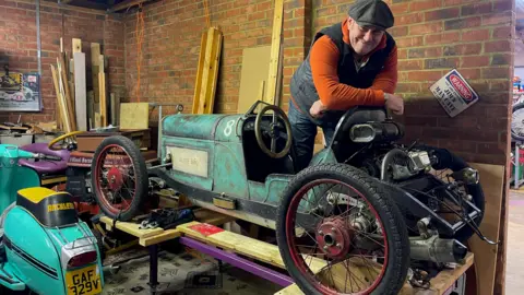 Engineer and motorsport enthusiast Jim Tanner leans on his homemade single-seat race car which is made from upcycled items including a broken shower dial in disguise as a black and gold centrepiece for the steering wheel