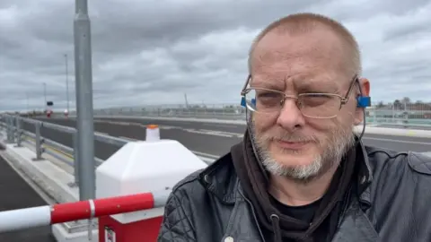 Andrew Turner/BBC Adam Marriner standing by the barrier on Herring Bridge