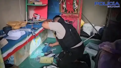 Policía Ecuador Police officer looking through items in a cell