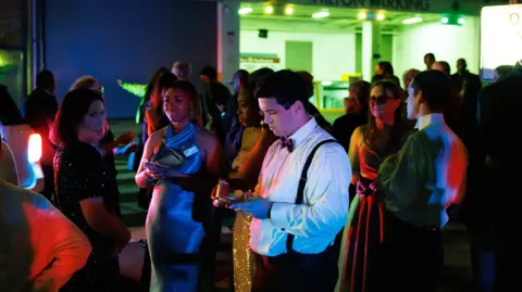 EPA Guests dressed in gowns and suits checking their phones and speaking to each other outside the venue.