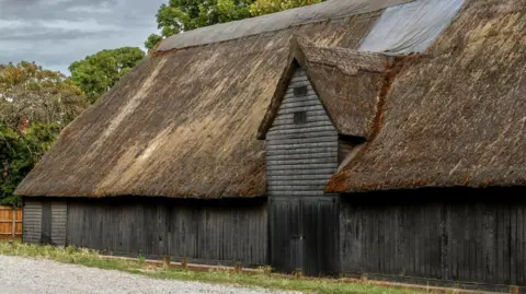 Historic England Archive An exterior view of the barn and its decaying thatch roof