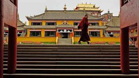 Xiqing Wang/ BBC A red-robed monk walks past the gates to a monastery in Aba 