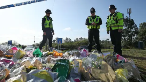 PA Media Three police officers stand by floral tributes to their colleague PC Andrew Harper