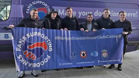 Fans Supporting Foodbanks Six men holding a banner for Fans Supporting Foodbanks. They are stood in front of a branded charity van and their banner reads: "Hunger doesn't wear colours".