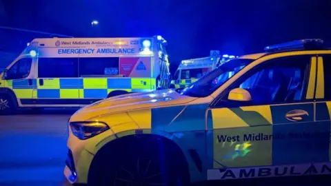 A 4x4 ambulance vehicle is pictured in front of two ambulances all with their blue lights flashing at night. 