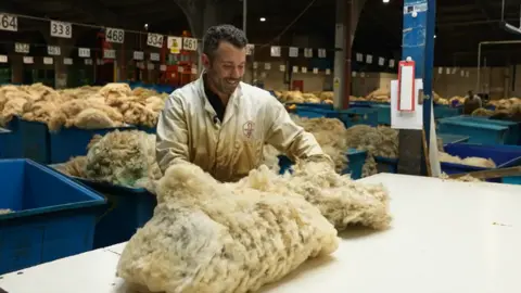 A man smiling in a white jacket looking and analysing a sheep fleece