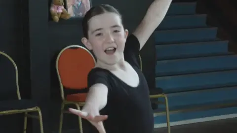 A young girl in a black leotard dancing
