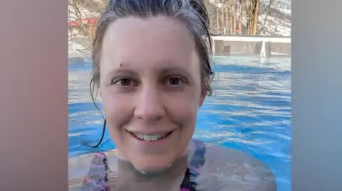 Daisy Brooks Daisy Brooks in an outdoor swimming pool with leafless trees and a snow-covered hillside behind her. Her hair is back from her face and she is beginning to smile. Her shoulders are under the water. She is wearing a pink and black swimming costume. 