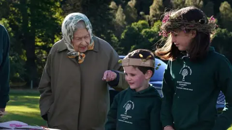 Getty Images Britain's Queen Elizabeth II interacts with school children from Crathie Primary before planting a tree at Balmoral Cricket Pavilion with Britain's Prince Charles, Prince of Wales, to mark the start of the official planting season for the Queen's Green Canopy (QGC), on the Balmoral Estate in Scotland on October 1, 2021.